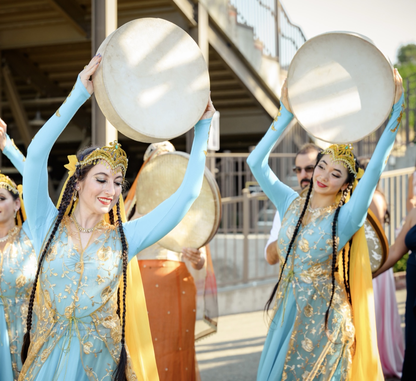 Dancers in blue and gold costumes raising daf drums overhead in a wedding procession