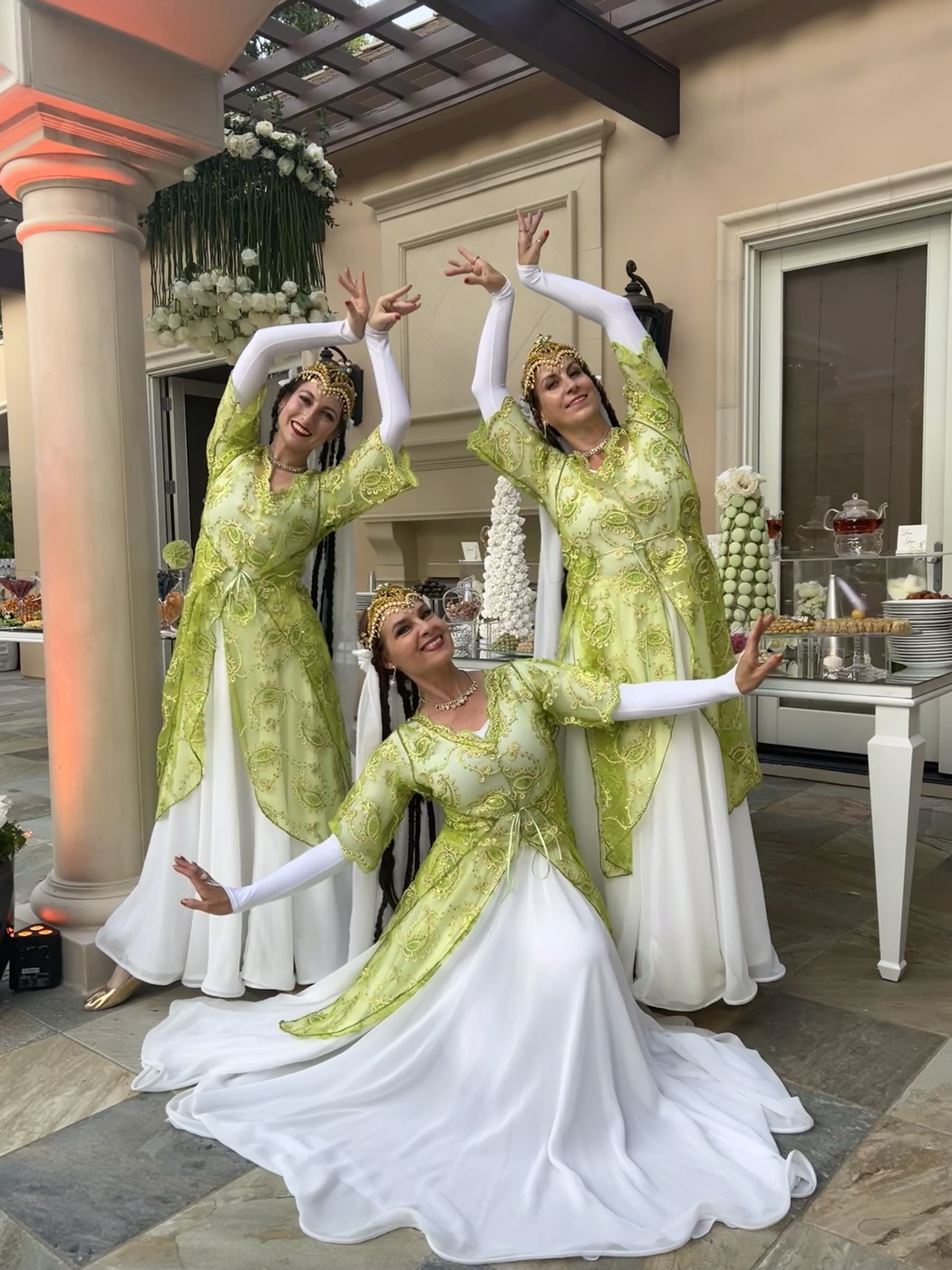 Three dancers in green and white Persian costumes posing at a wedding reception